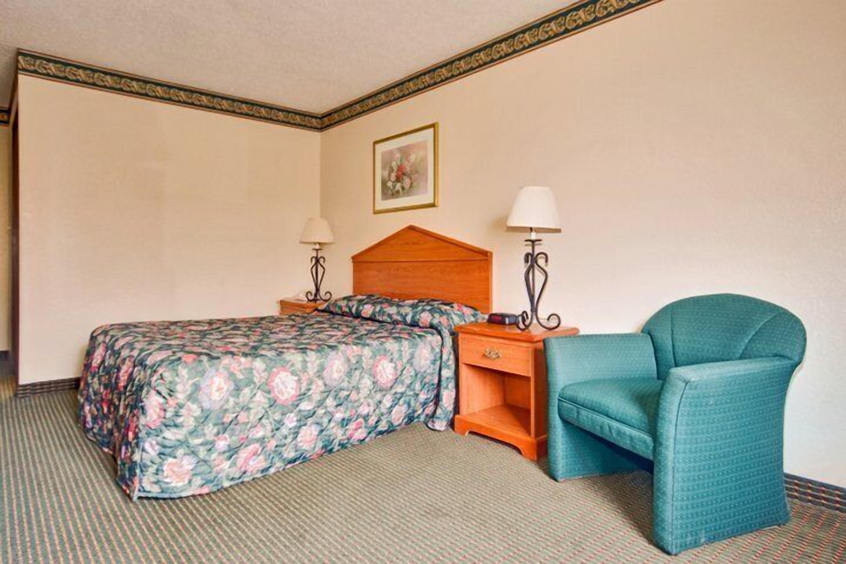 A hotel room with a bed, a chair, a nightstand, and two lamps.
