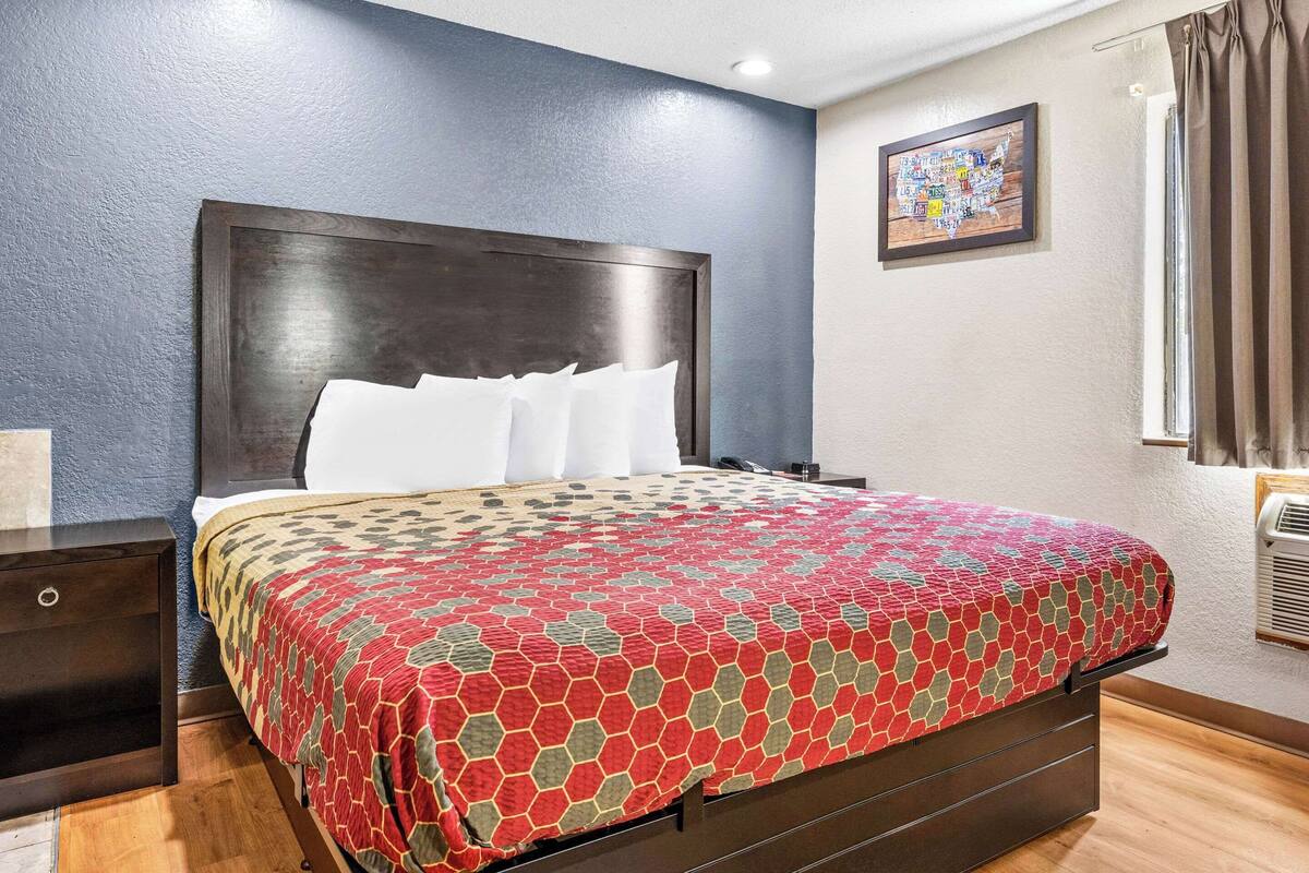 Ein Hotelzimmer mit einem großen Bett, einem Nachttisch aus Holz, einer wandmontierten Klimaanlage und einer gerahmten Karte an der Wand.