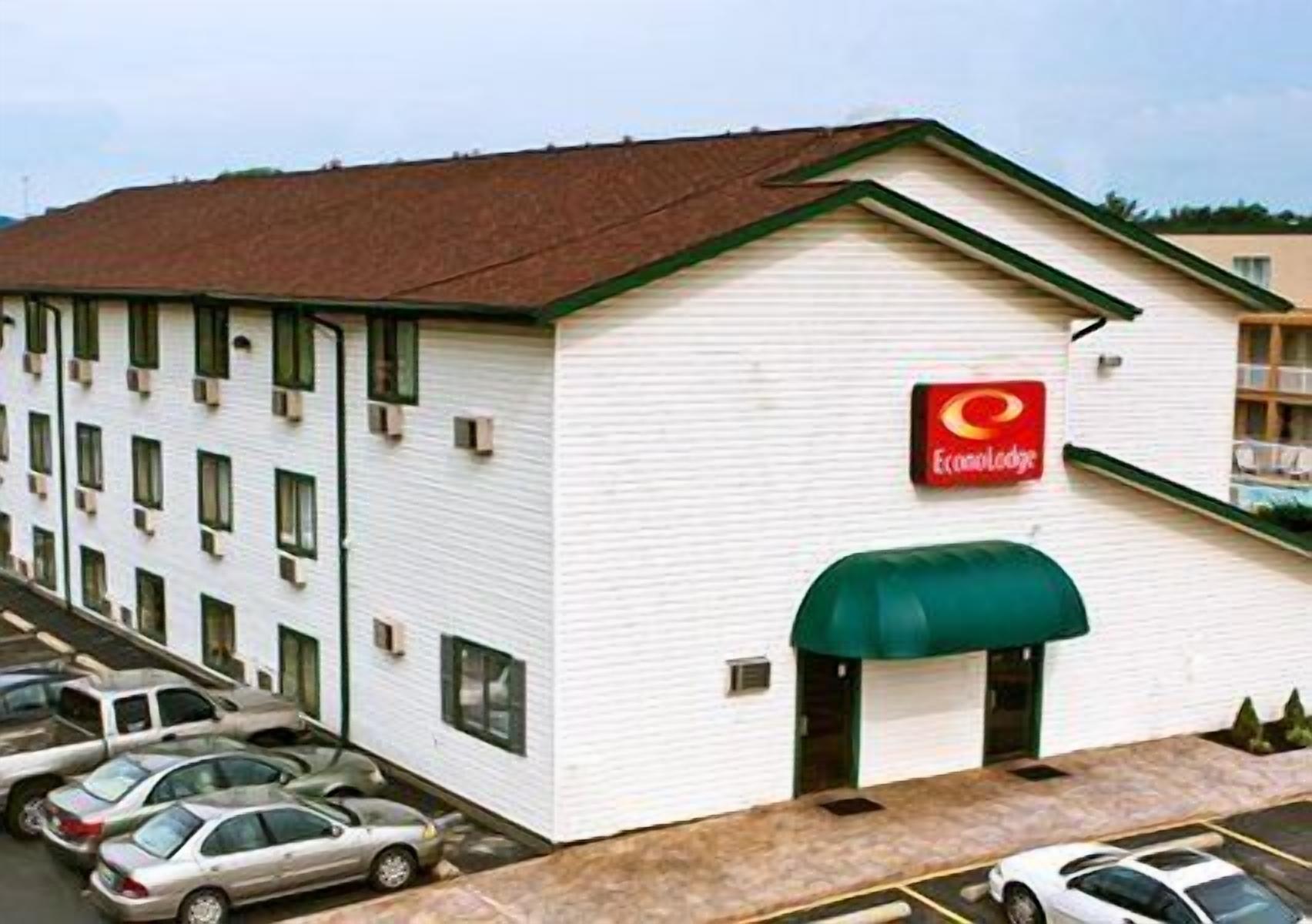 A white building with a green awning and a red logo. There are multiple windows and a parking lot with cars.