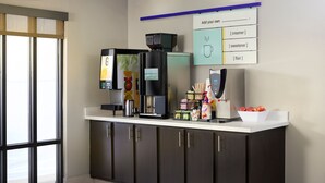 A modern coffee station with a coffee machine, a tea dispenser, and a menu board.