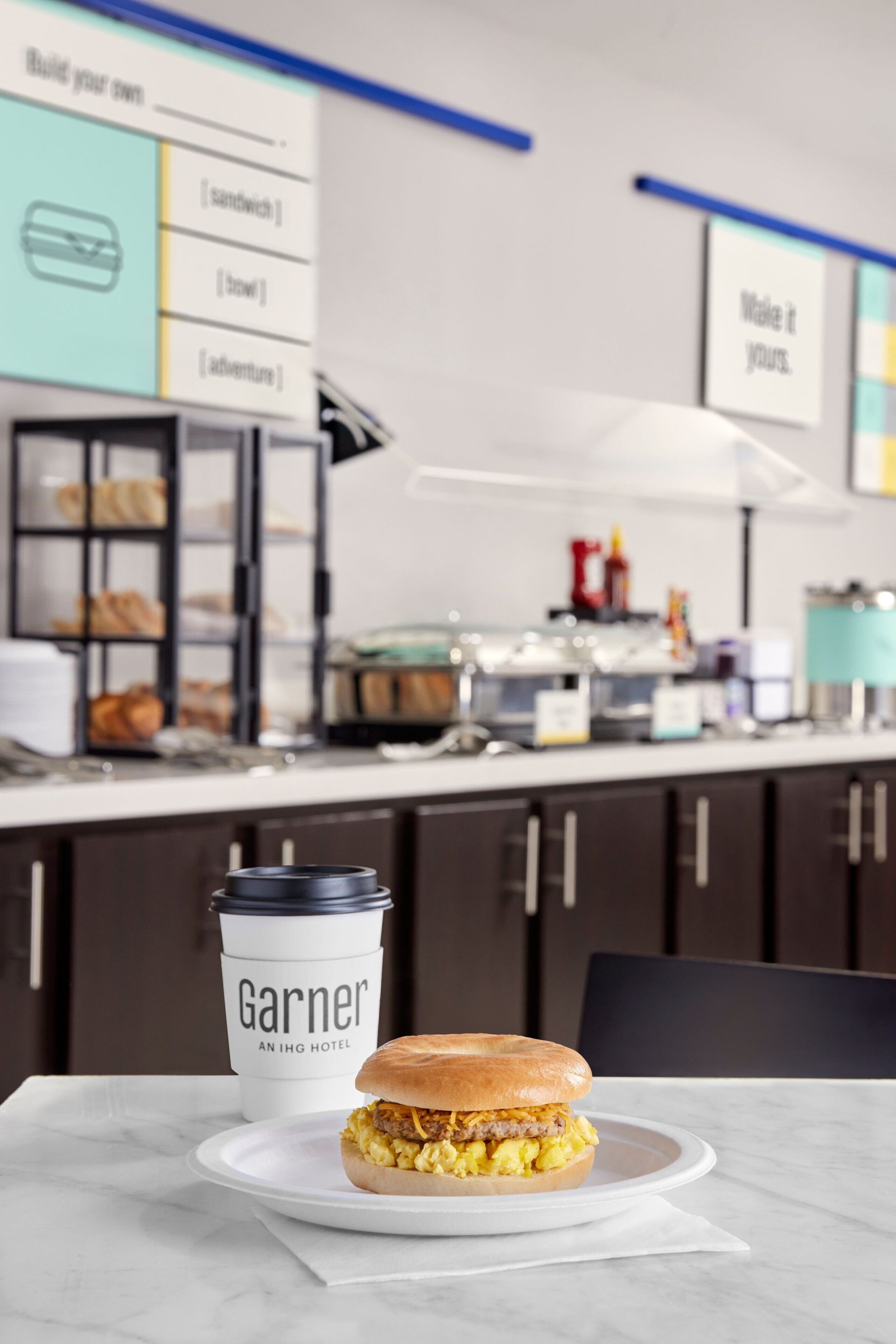 A breakfast sandwich on a plate with a coffee cup labeled 'Garner' in a hotel setting.