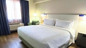A hotel room with a large bed, a desk, a chair, and a window with curtains.