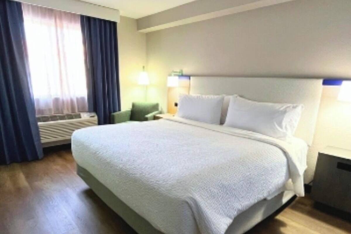 A hotel room with a large bed, a desk, a chair, and a window with curtains.