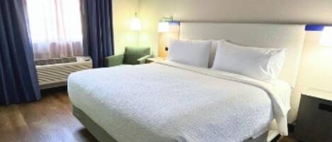 A hotel room with a large bed, a desk, a chair, and a window with curtains.