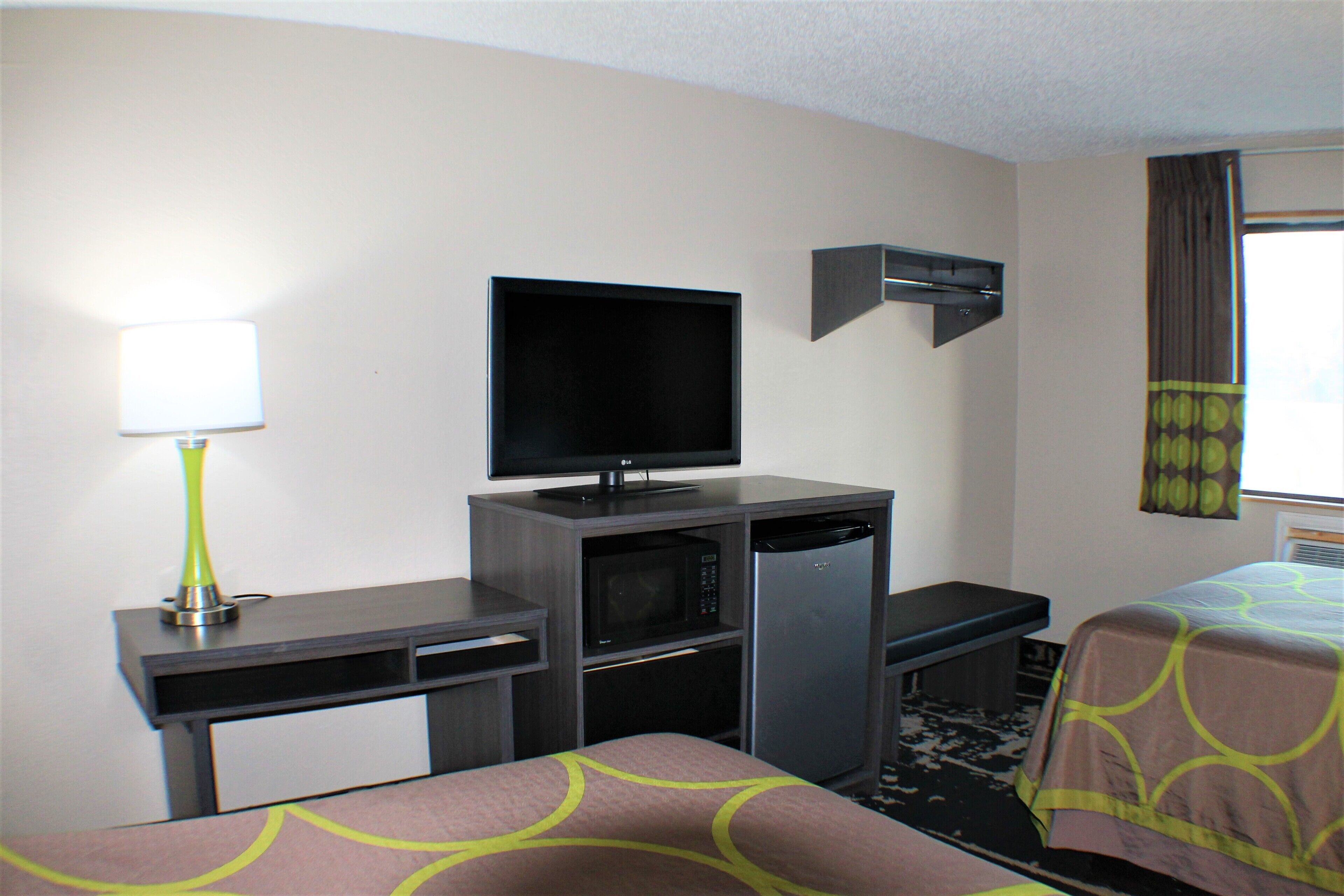 Una habitación de hotel con cama, escritorio, televisión, microondas y refrigerador.