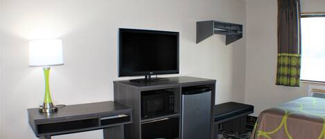 A hotel room with a bed, a desk with a television, a microwave, and a refrigerator.