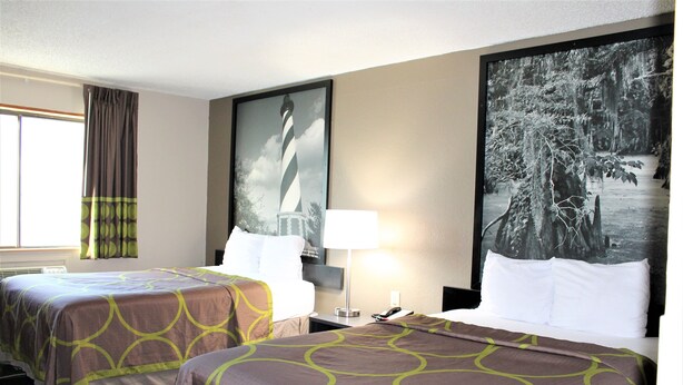 Habitación de hotel con dos camas, un cuadro grande con un faro, una lámpara y una ventana con cortinas.