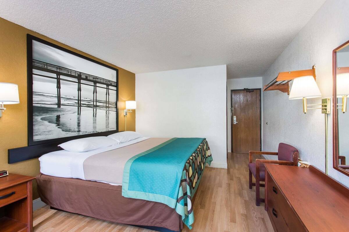 Une chambre d’hôtel avec un lit, un bureau, une chaise, un grand miroir et une porte.