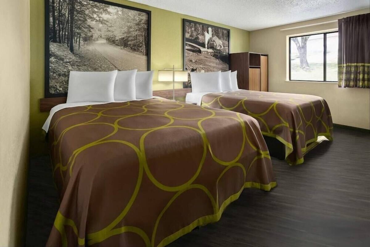 A hotel room with two beds, a nightstand, a lamp, and a window with curtains.