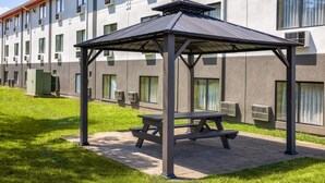 A covered outdoor seating area with a picnic table in front of a modern building with multiple windows and air conditioning units. - Super 8 by Wyndham St. Clairsville OH/Wheeling WV Area (St. Clairsville)