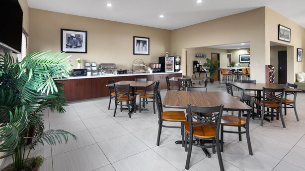 A spacious dining area with multiple tables and chairs, a coffee station, and potted plants. - Super 8 by Wyndham St. Clairsville OH/Wheeling WV Area (St. Clairsville)