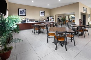 Un comedor amplio con varias mesas y sillas, una estación de café y plantas en macetas.