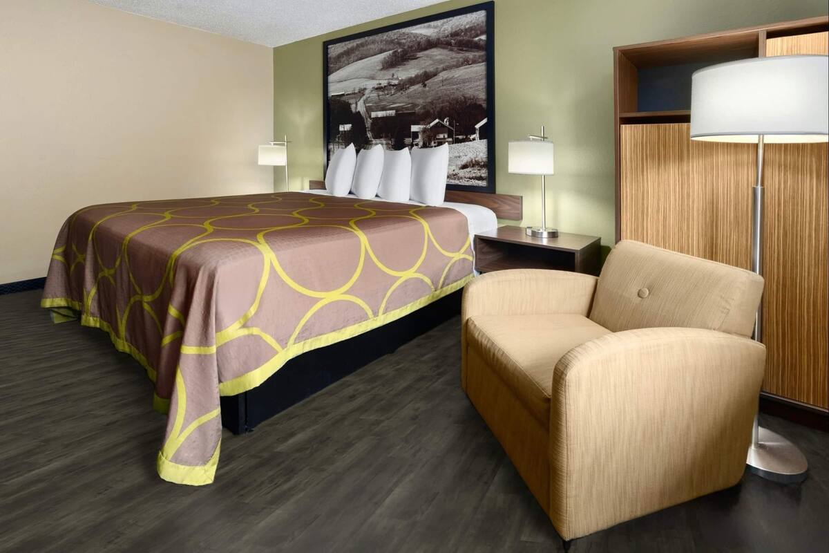 A hotel room with a bed, a chair, a nightstand, and a lamp.