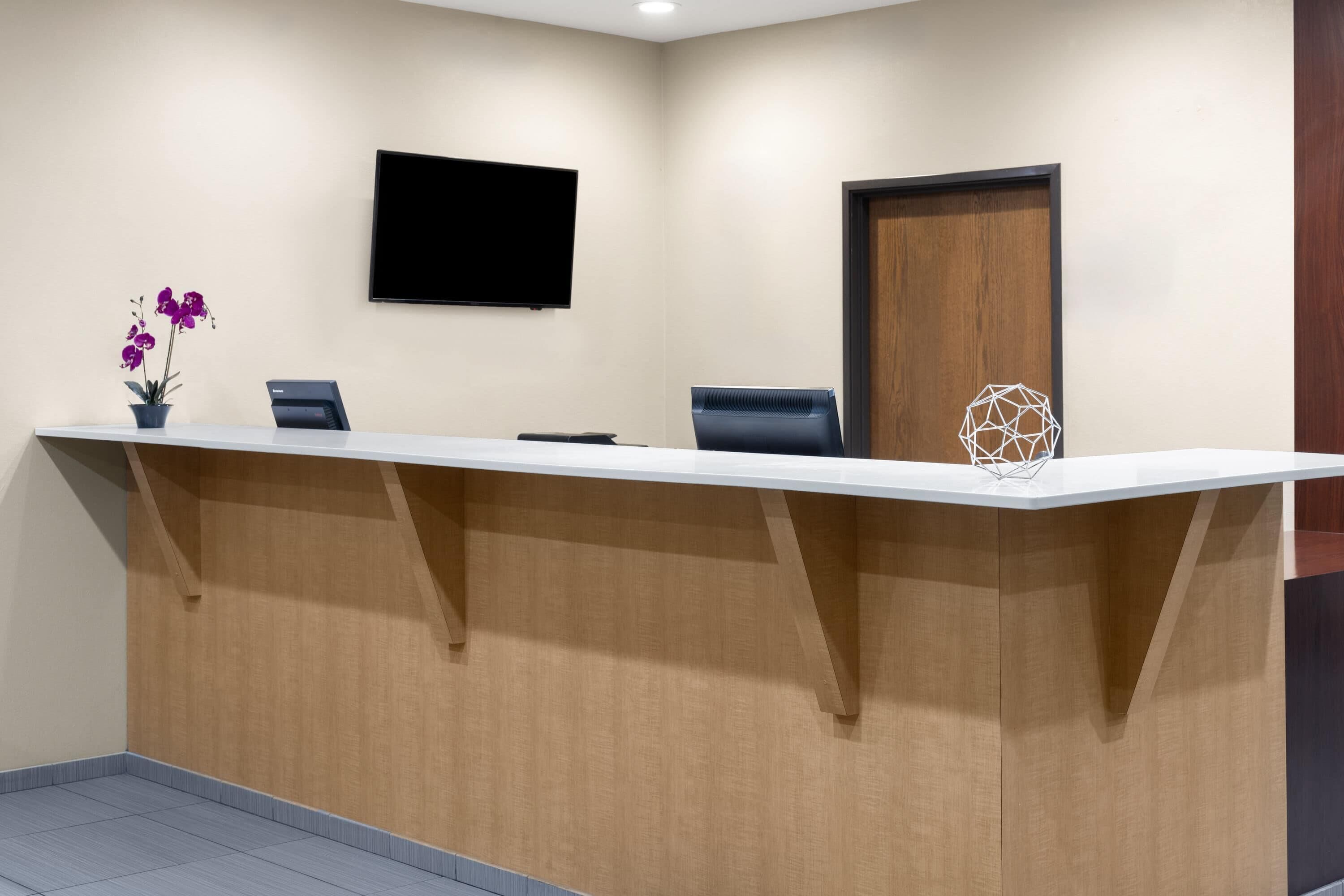 Un mostrador de recepción con un televisor de pantalla plana, una puerta de madera y una pieza decorativa geométrica.