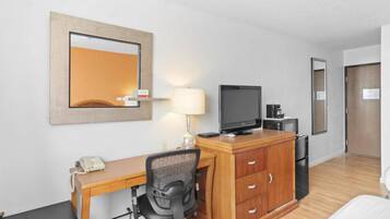 Habitación de hotel con escritorio de madera, una silla, televisor, lámpara, teléfono y armario.