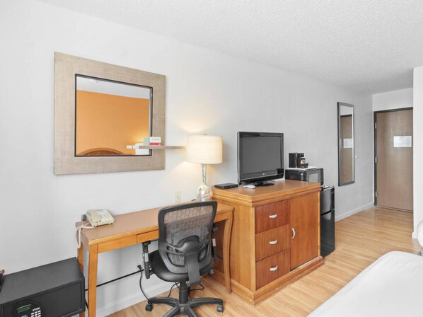 A hotel room with a wooden desk, a chair, a television, a lamp, a telephone, and a wardrobe.