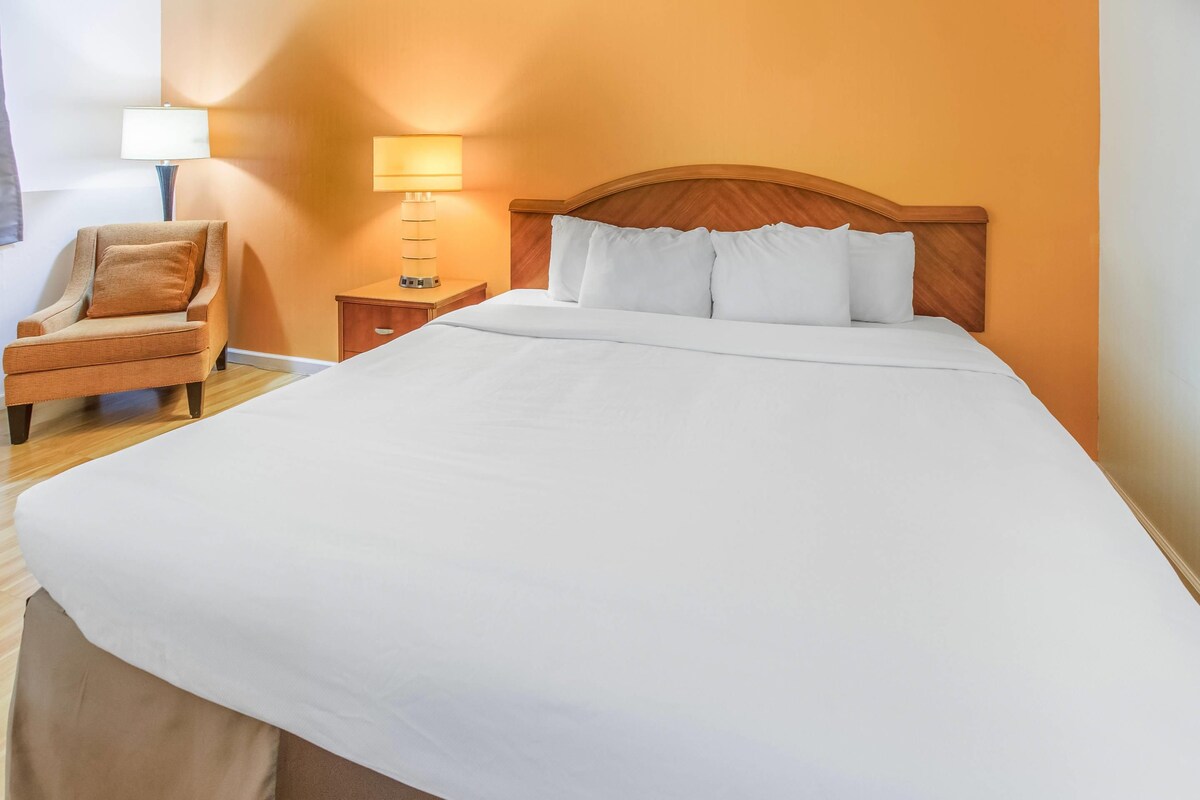 Una habitación de hotel con una cama grande, una silla, una mesita de noche y una lámpara.