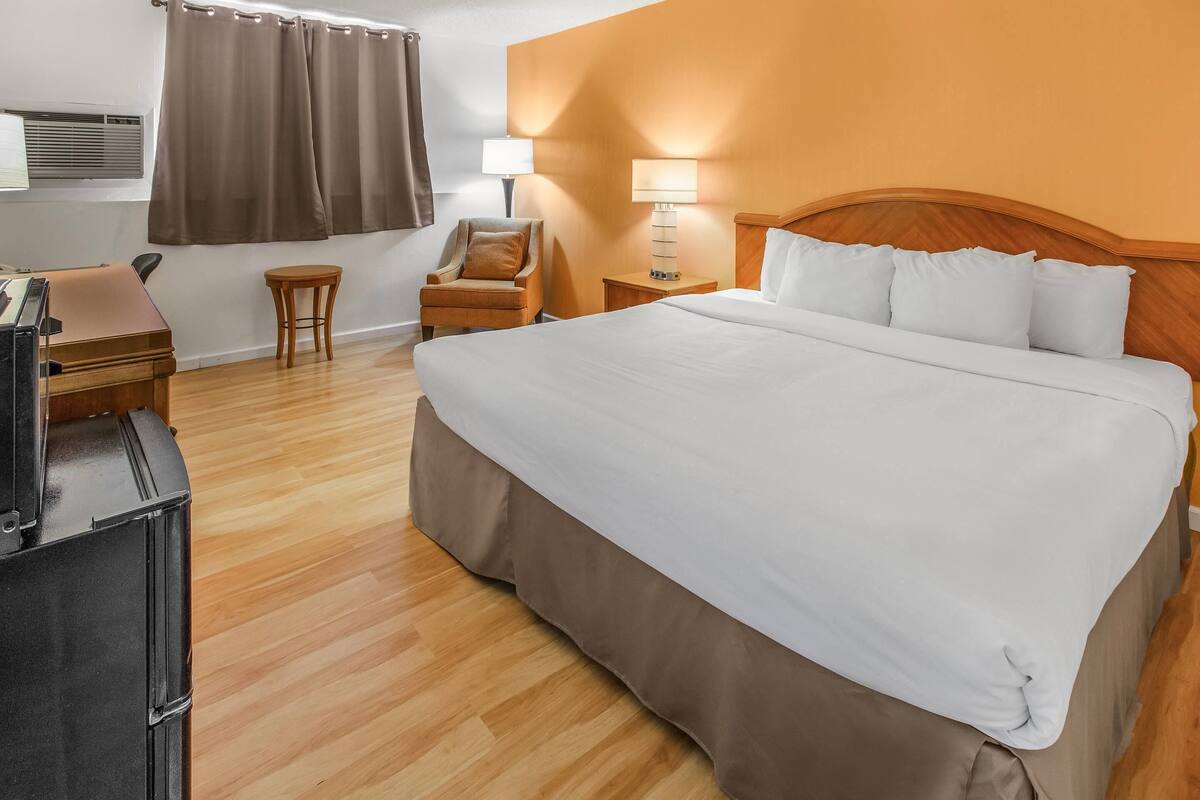 Ein Hotelzimmer mit Bett, Schreibtisch mit Computer, Stuhl, Lampe und Klimaanlage.