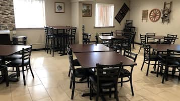 A dining area with multiple tables and chairs, a tiled floor, and framed artwork on the walls.