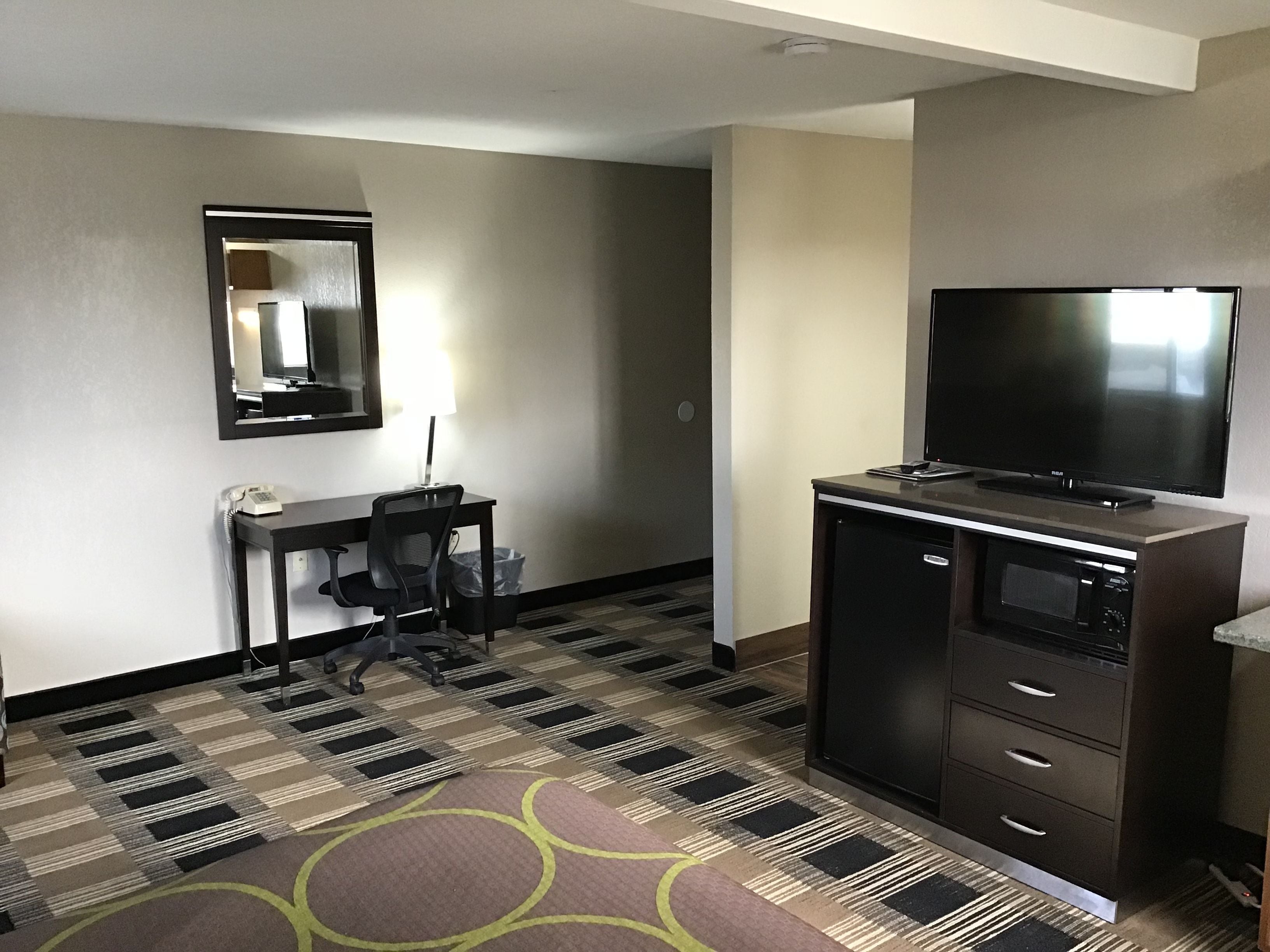 A hotel room with a desk, chair, television, and a microwave.