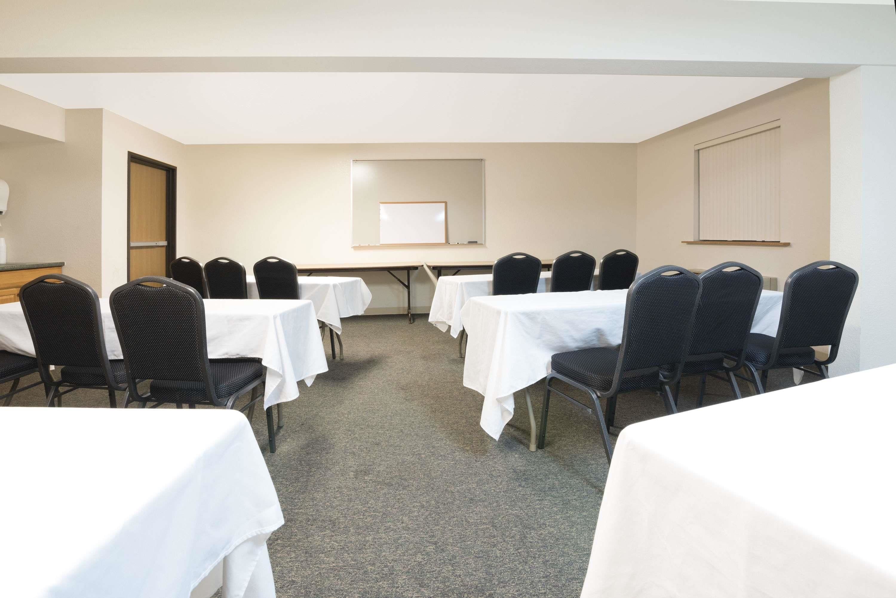 A conference room with multiple tables and chairs, a whiteboard, and a door.