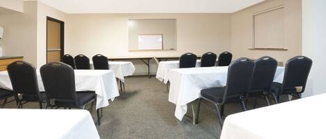 A conference room with multiple tables and chairs, a whiteboard, and a door.