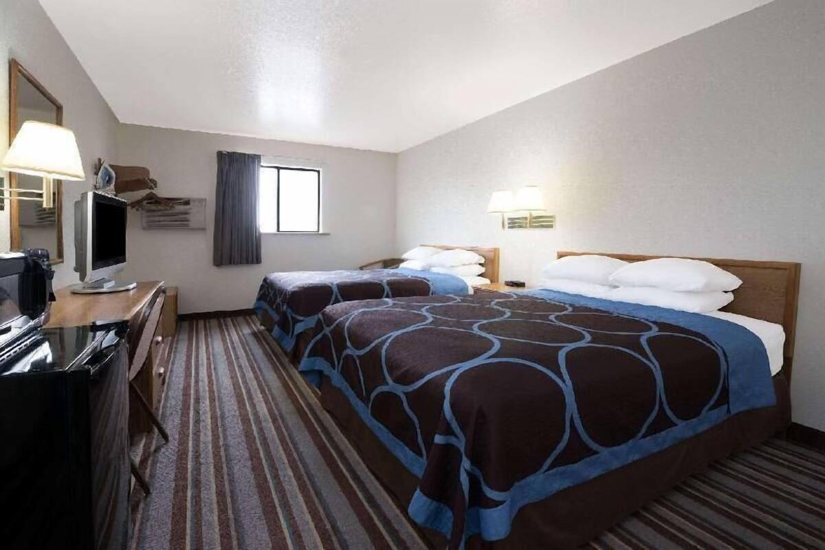Hotelkamer met twee bedden, een bureau met een computer, een televisie en een raam met gordijnen.