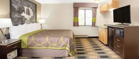 Una habitación de hotel con cama, televisión, kitchenette y un gran ventanal con cortinas.