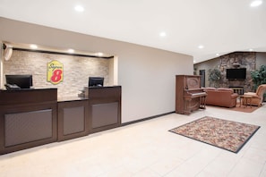 Una zona de recepción con pared de piedra, un letrero de Super 8, un mostrador de recepción, un piano y un área de descanso con televisor.
