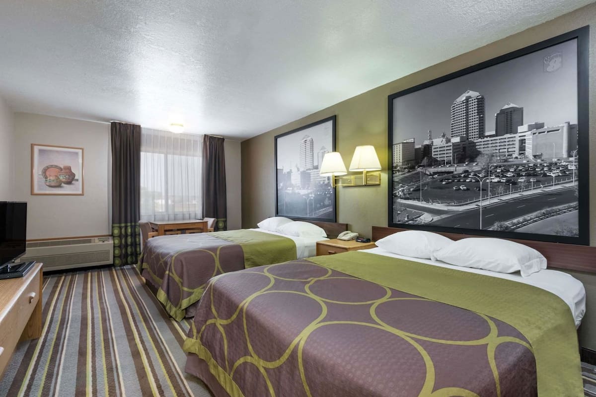 A hotel room with two beds, a desk, a chair, a TV, a window with curtains, and a cityscape view.