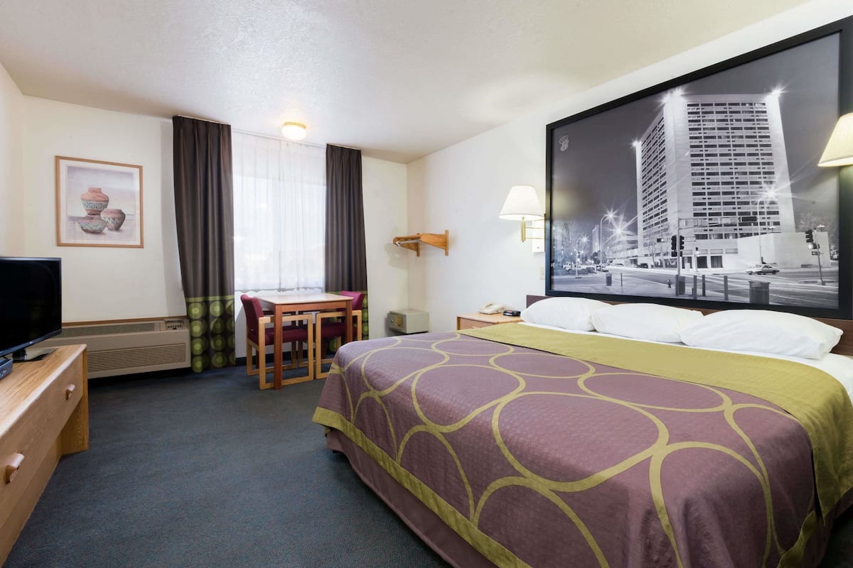 A hotel room with a bed, a desk, a chair, a television, and a large window with a cityscape view.
