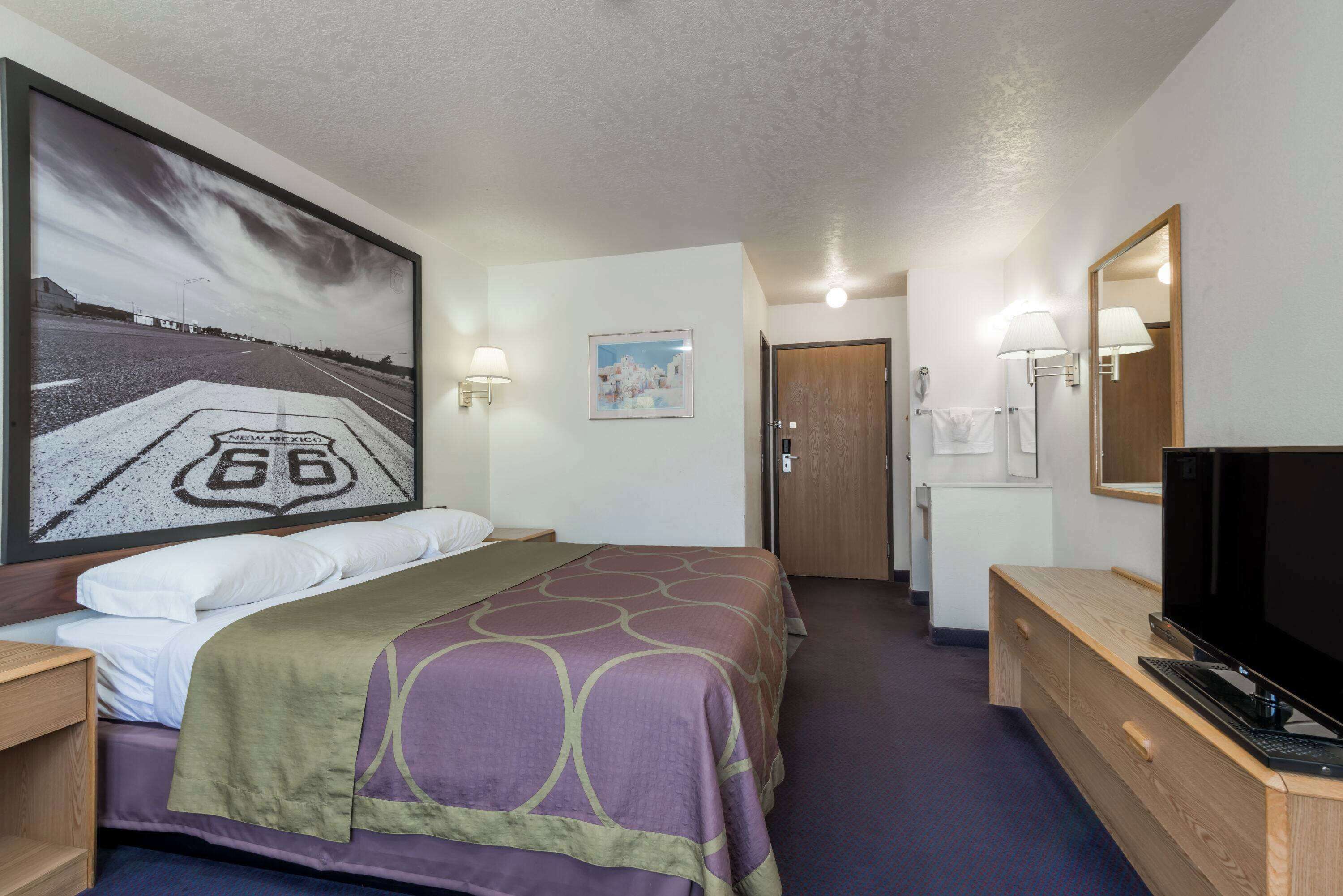 A hotel room with a bed, a television, a desk, and a painting of a road sign.