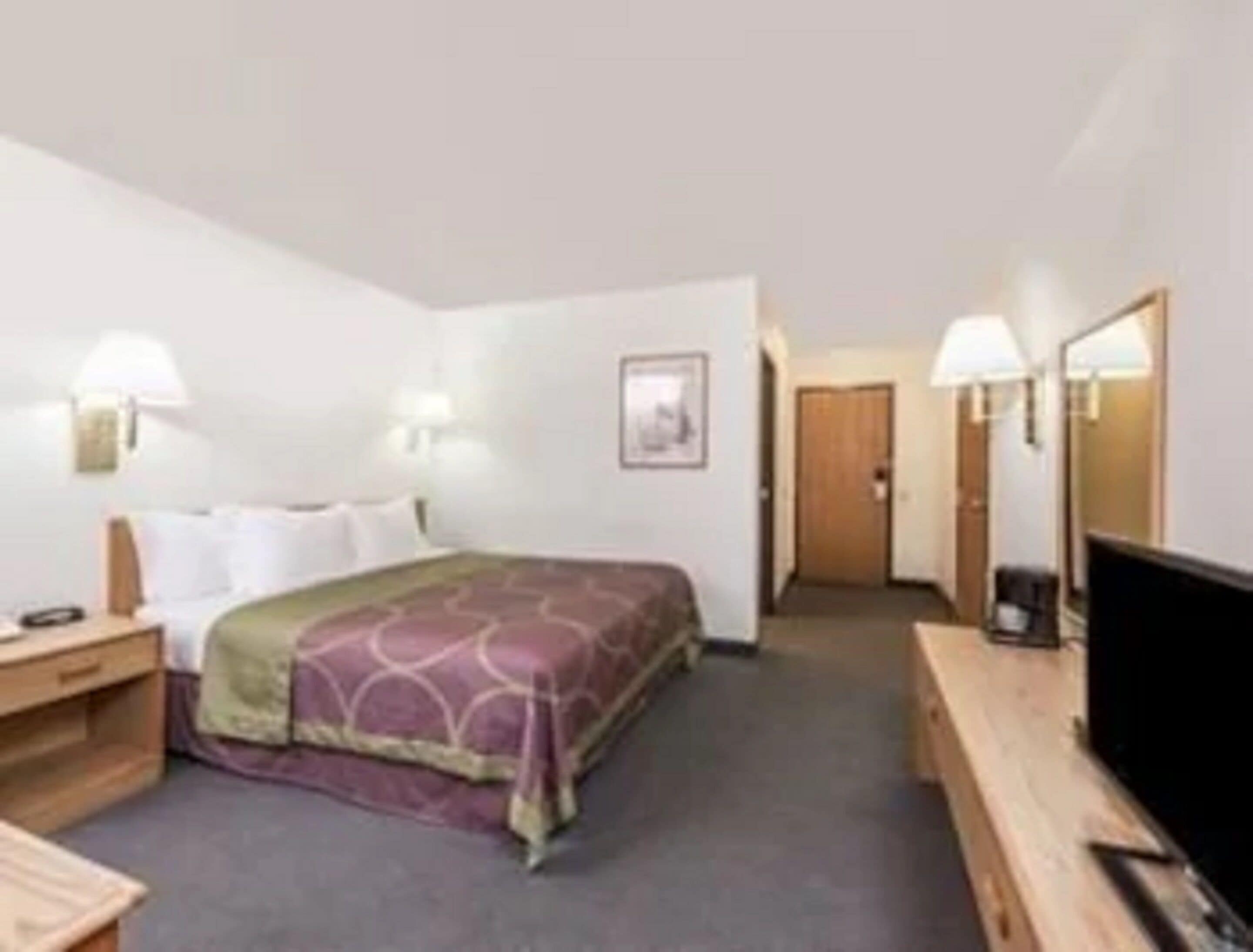 A hotel room with a bed, bedside tables, a TV, and a door leading to another room.