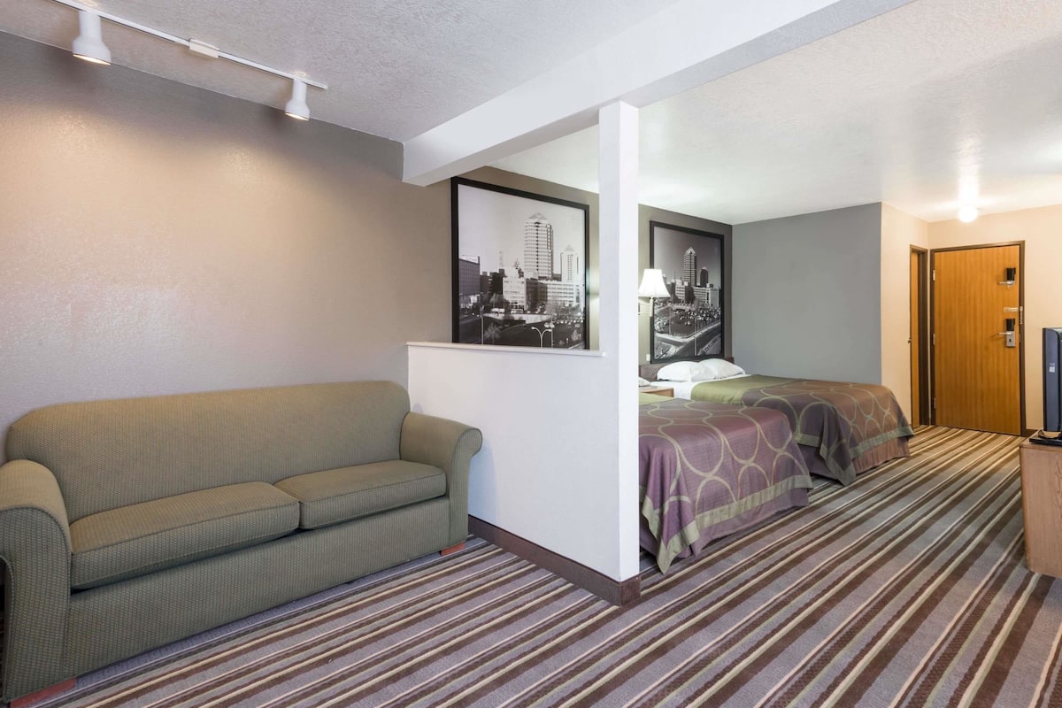 A hotel room with a single bed, a sofa, a framed cityscape picture, and a door.