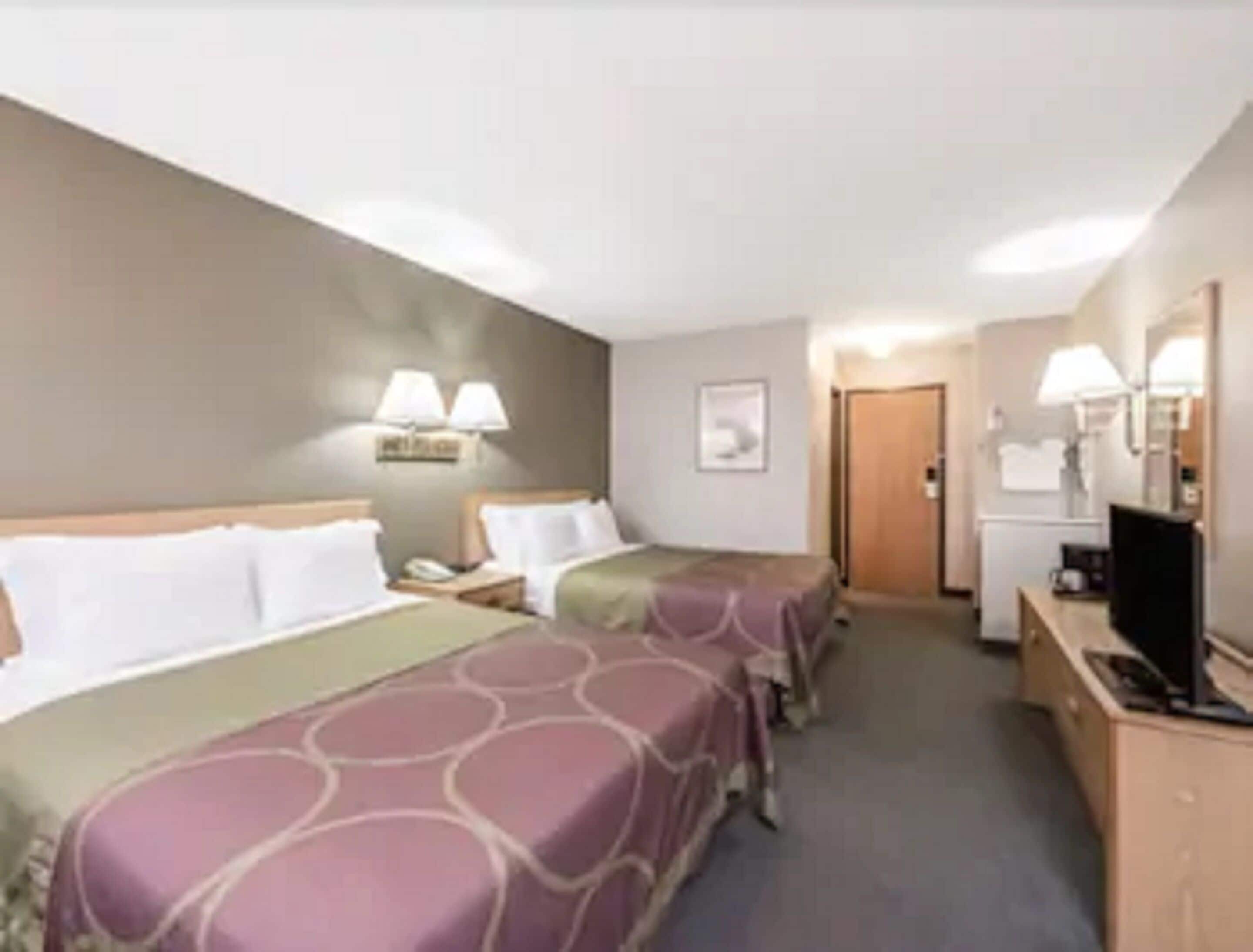 A hotel room with two beds, a desk with a computer, a TV, and a door leading to another room.