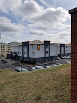 Un hotel de diseño moderno, con un llamativo letrero de 'Super 8'. Cuenta con un estacionamiento con varios autos y un área verde al frente.