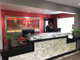 A hotel reception desk with a marble counter, a red wall with a cityscape mural, and a receptionist standing behind the desk.