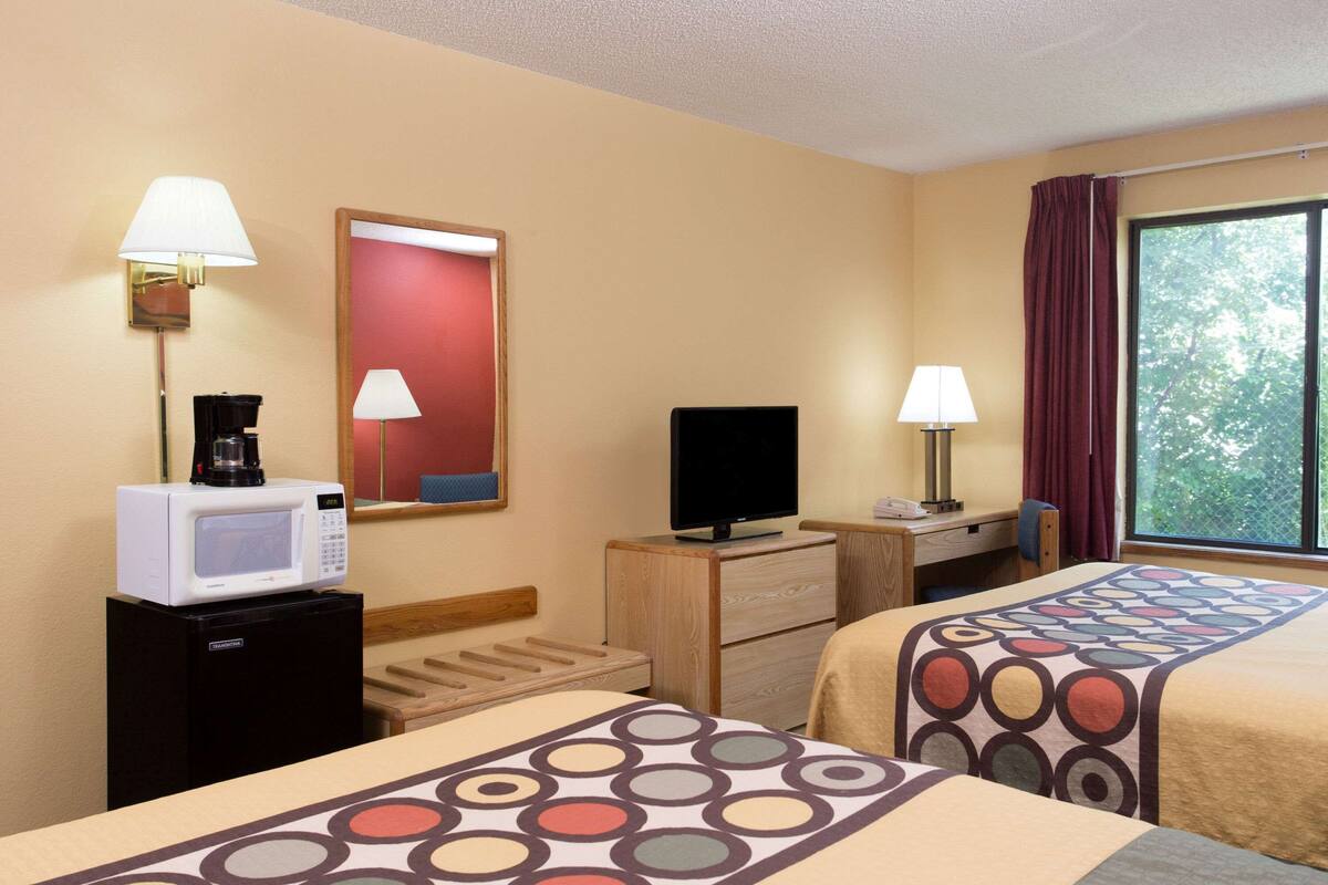 Habitación de hotel con dos camas, televisión, microondas, cafetera y ventana con cortinas.
