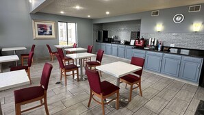 A modern dining area with tables and chairs, a kitchen with a brick backsplash, and a clock on the wall.