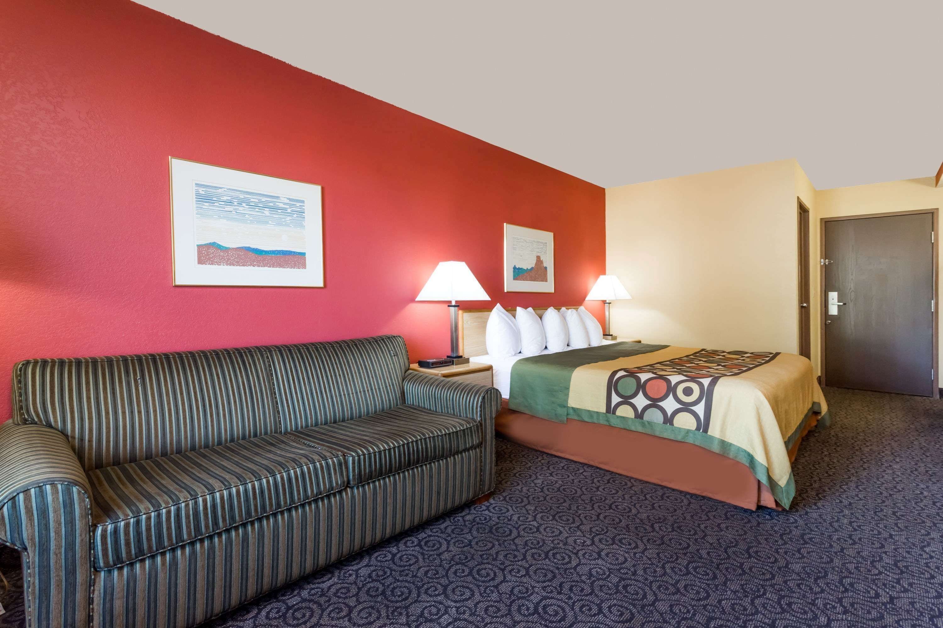 A hotel room with a striped sofa, a bed with a patterned bedspread, two wall-mounted lamps, and two framed pictures.