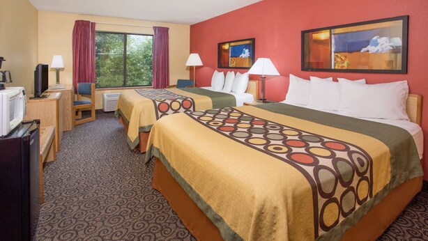 A hotel room with two beds, a desk, a television, and a window with curtains.