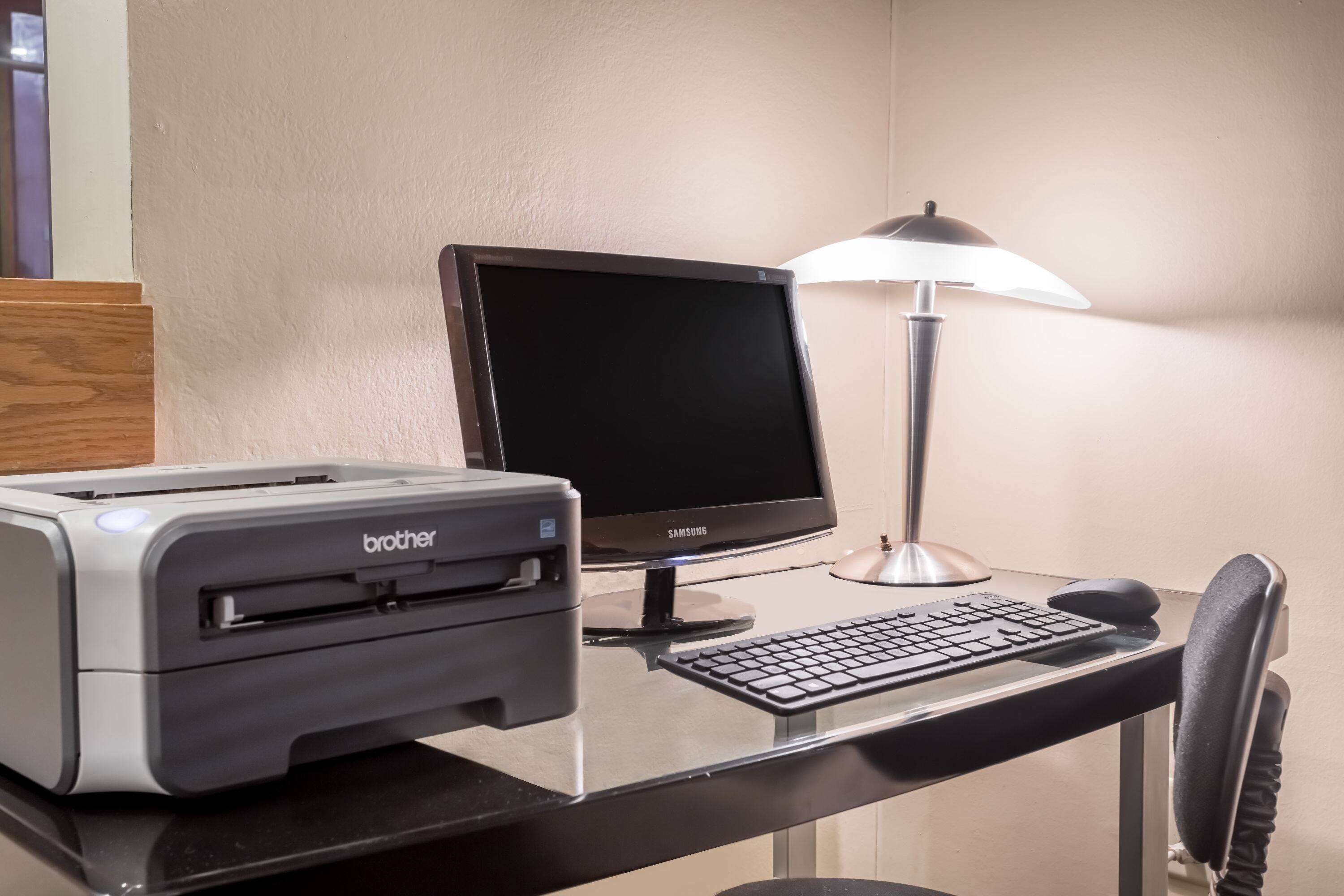 A desk with a Brother printer, a Samsung monitor, a keyboard, a mouse, and a lamp.