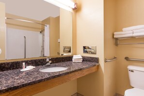 A bathroom with a granite countertop, a sink, a mirror, a toilet, and a towel rack.