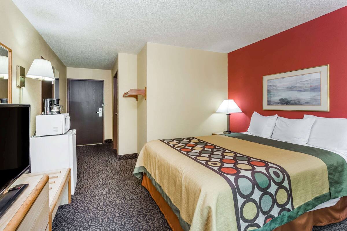 Una habitación de hotel con cama, escritorio, computadora, microondas y televisión.