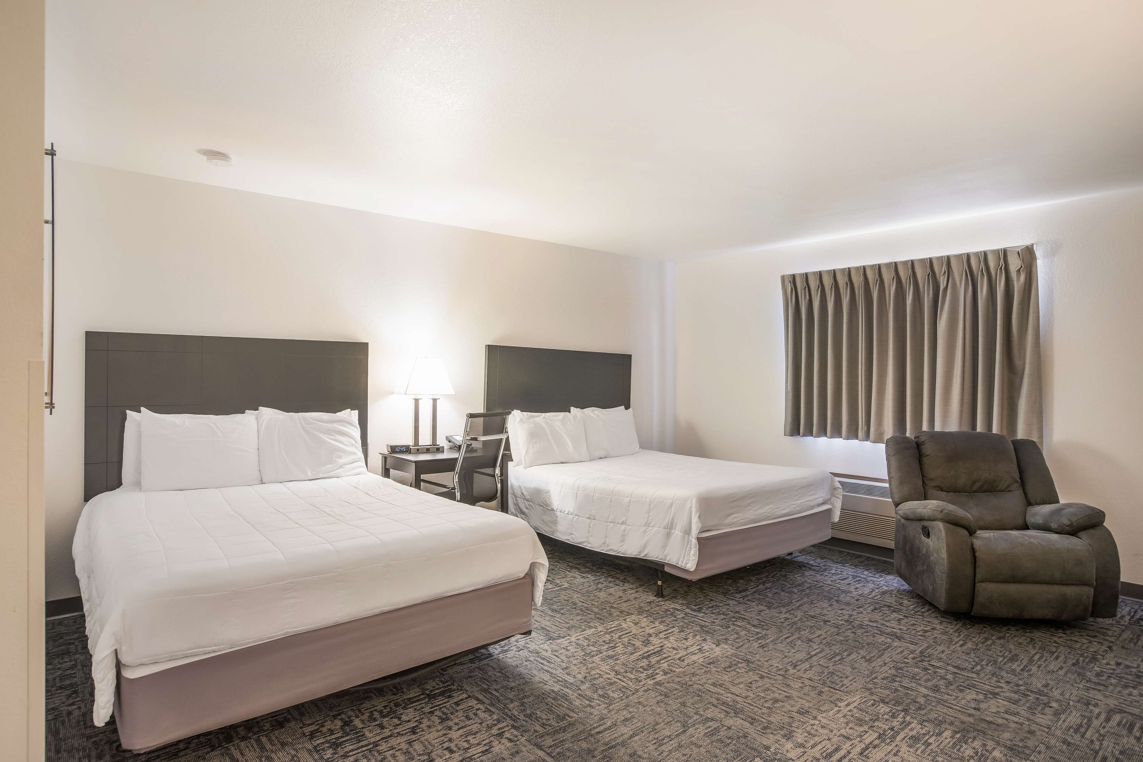 Quarto de hotel com duas camas, uma cadeira, uma escrivaninha e uma janela com cortinas.