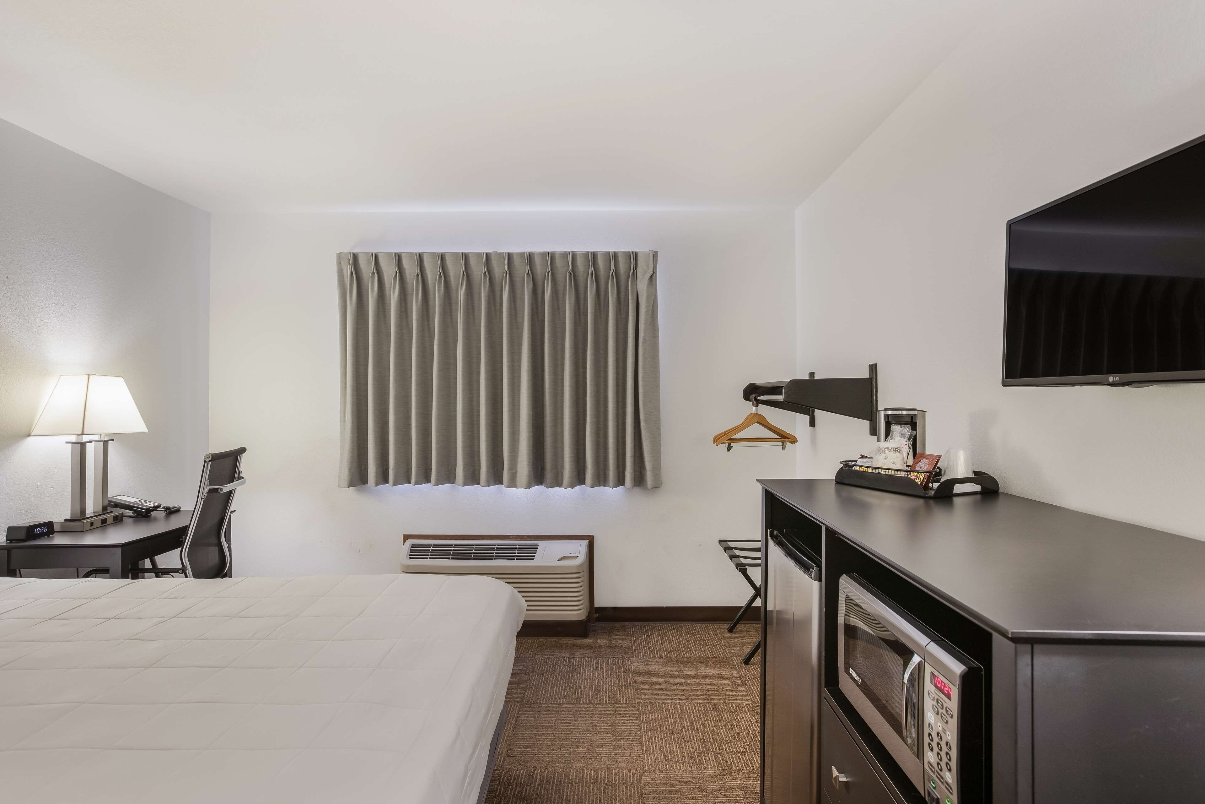 A hotel room with a bed, desk, chair, TV, and a microwave.