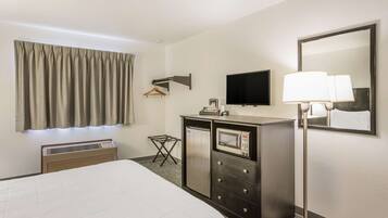 Une chambre d’hôtel équipée d’un lit, d’un bureau avec un micro-ondes, d’une télévision, d’une lampe et d’un miroir.