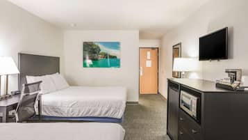 Una habitación de hotel con cama, escritorio y silla, televisor, cómoda y puerta.