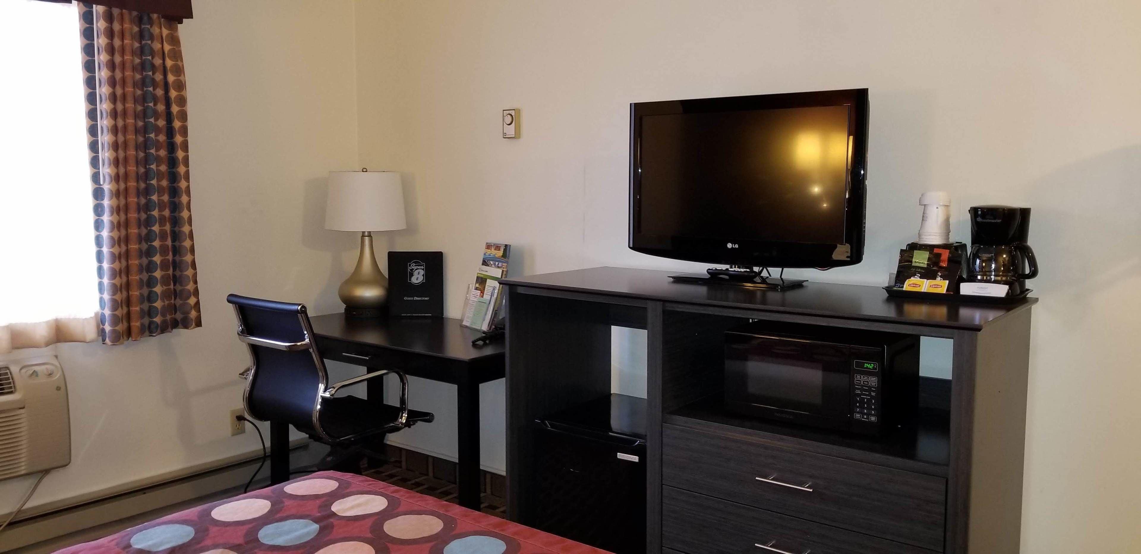 Une chambre d’hôtel équipée d’un lit, d’un bureau avec un ordinateur, d’un téléviseur à écran plat, d’une lampe, d’une machine à café et d’un four à micro-ondes.