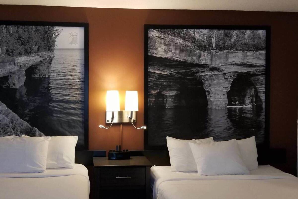 Une chambre d’hôtel avec deux lits, une table de chevet et une lampe fixée au mur.